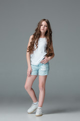 Full length of young slim female girl in denim shorts on gray background