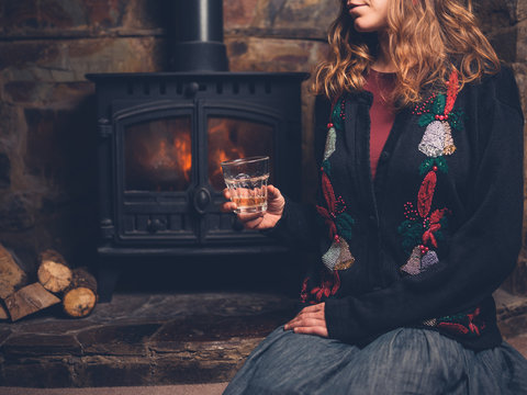 Woman in christmas jumper with drink by fire