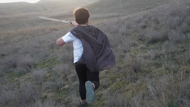 A boy with a sword runs to the horizon at sunset. Slow Motion video