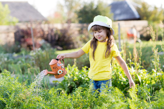 Little kid girl watering plants with can in a garden