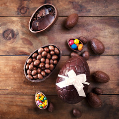 Chocolate Easter eggs on wooden background with ribbon bow and candies.