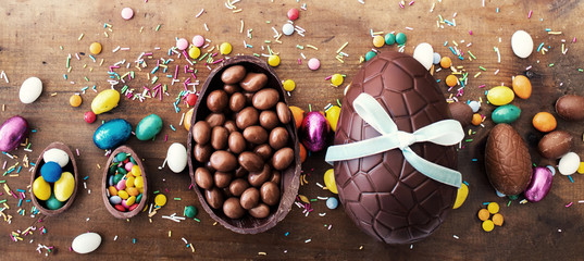 Chocolate Easter eggs on wooden background with ribbon bow and candies.