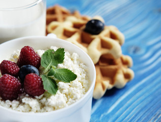 Cottage cheese with berries, waffles and milk on a wooden blue b