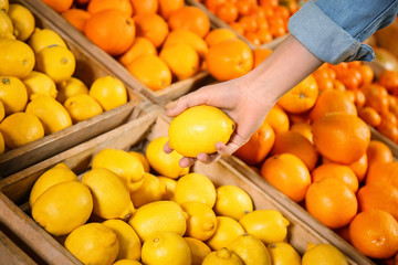 Young woman choosing fresh lemons in supermarket