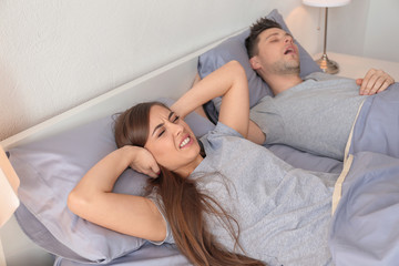 Young irritated woman lying in bed with snoring husband at home