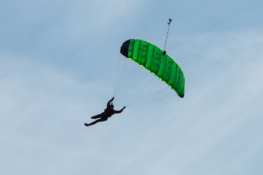 Parachutist with Green Parachute against Clear Blue Sky