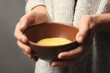 Poor woman holding bowl with corn grits, closeup