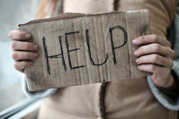 Poor woman holding piece of cardboard with word HELP, closeup