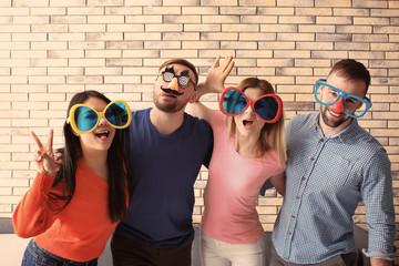 Young people in funny disguise posing on brick wall background. April fool's day celebration