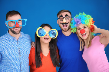 Young people in funny disguise posing on color background. April fool's day celebration