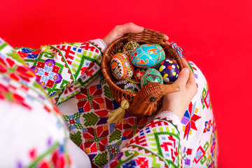 Multi-colored Easter eggs lie in a wicker vase in the hands of the girl.