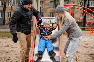 Cute toddler boy playing with father and mother on the playground