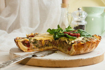 French opened pie quiche with tuna / chicken, broccoli, spinach, pepper, eggs, cheese and dried tomato on white wooden background.