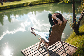 Young woman sitting on chair and relax on the lake coast in the park