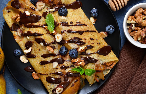 Homemade thin pancakes with caramelized pears, chocolate sauce and nuts on a concrete background.