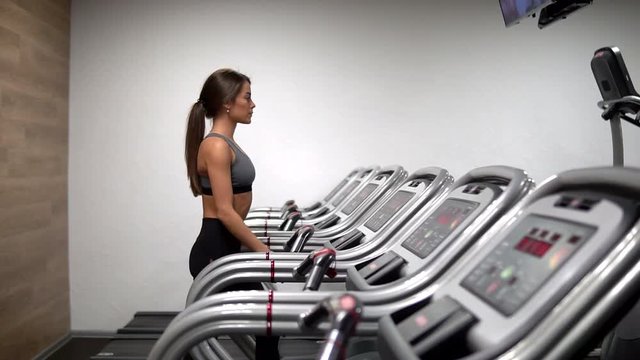 Attractive girl running on the treadmill in the gym. profile face shot. Slow mo