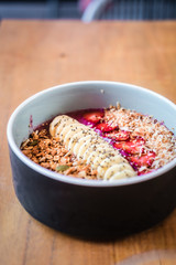 Dragon fruit smoothie bowl with banana, strawberries, granola, coconut milk from above. Wooden table at coffee shop. Minimalist food photography