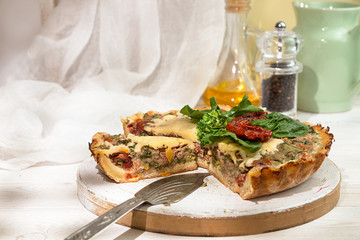 French opened pie quiche with tuna / chicken, broccoli, spinach, pepper, eggs, cheese and dried tomato on white wooden background.