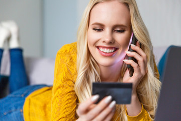 close-up view of smiling blonde girl holding credit card and talking by smartphone