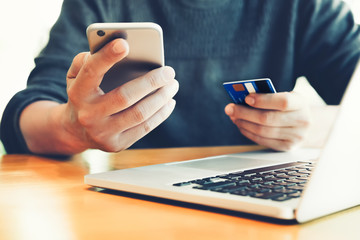 online payment and shopping, Young man holding smartphone and creditcard and using computer laptop for purchase to item on internet.