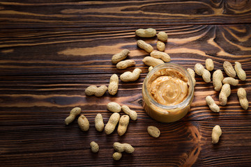 Bowl of peanut butter and peanuts on dark wooden background from top view. Space for text or design.
