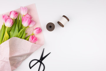 Minimal styled flat lay with pink tulips flowers with petals in pink paper wrapper, two thread spool and black scissors. Mock up top view isolated on white. Feminine flat lay.