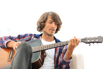 Handsome man playing on the guitar on the couch at home
