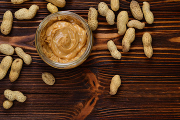 Bowl of peanut butter and peanuts on dark wooden background from top view. Space for text or design.