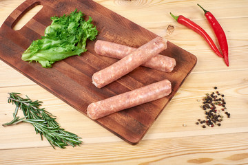 Raw sausages with vegetables and spices on wooden background