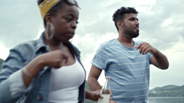 Group of friends holding drinks, enjoying music and doing silly dances at summer outdoor party