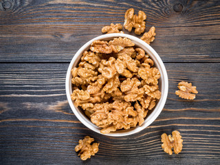 Top view of glass jar with a handful of walnut, circassian nuts on a wooden dark background.