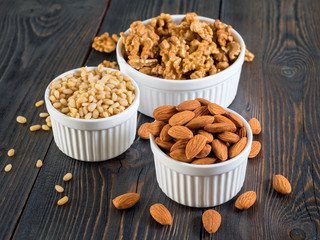 assorted nuts in white bowl on wooden dark background, mix of walnuts, almonds and cedar, side view