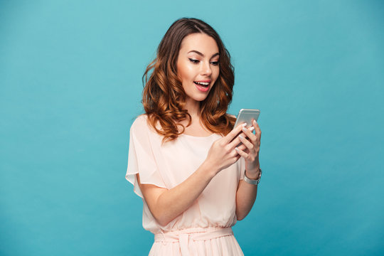 Image of cheerful woman 20s smiling and using mobile phone while virtual communicating, isolated over blue background