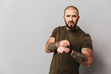 Portrait of male bodybuilder in casual t-shirt posing on camera using smartwatch on wrist, isolated...