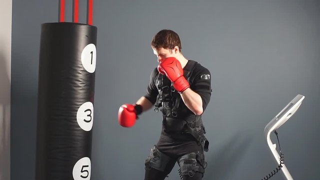 Fit man in boxing gloves during training. Boxer in suit of electric stimulation in gym.