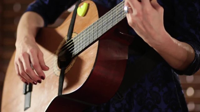 Hands on the strings of an acoustic guitar. Close-up. A girl in a blue dress completes the game on a musical instrument.