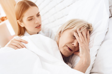 Girl is nursing elderly woman at home. Woman is feeling bad, girl is concerned.