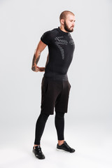 Fototapeta premium Full-length portrait of strong-willed tattooed man in black sportswear stretching his arms while workout, isolated over white background