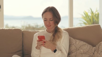 Happy woman using smart phone for downloading mobile app in home interior