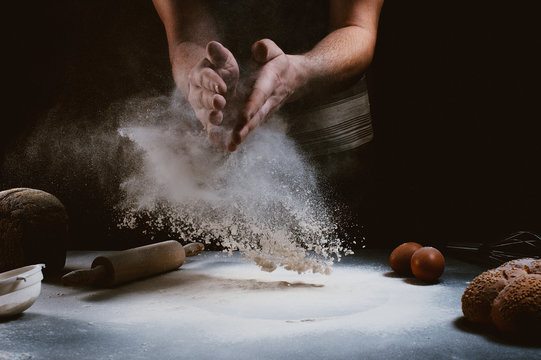 hand of chef clap a flour with wooden rolling pin and ingredients on dark background
