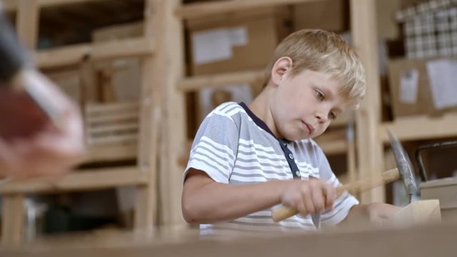 Boy of primary school age working in art studio and using hammer to drive nails into block of wood