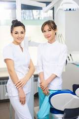 Cheerful group of young dentists and their assistants standing in the dental office and looking at camera and friendly smiling at white background of medical room.