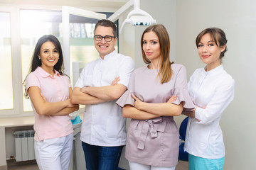 Cheerful group of young dentists and their assistants standing in the dental office and looking at camera and friendly smiling at white background of medical room.