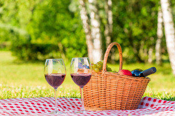 Fototapeta na wymiar wicker basket for a picnic with fruit and red wine on a tablecloth in a park for two lovers
