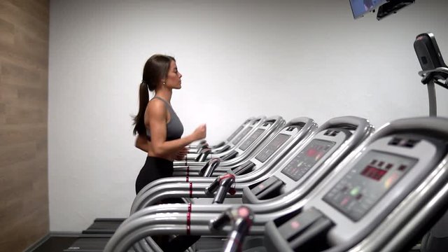 Attractive girl running on the treadmill in the gym. profile face shot