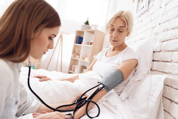 Obraz premium Girl is nursing elderly woman at home. Girl is using tonometer to measure blood pressure.