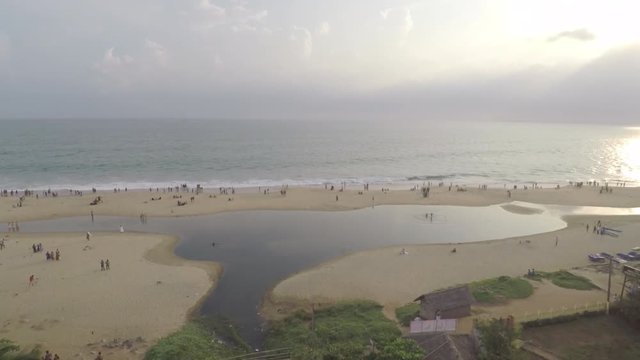 An aerial view of a tropical beach in Kerala, India with coconut trees and people walking at the shore.