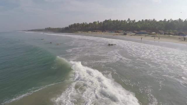 A beautiful looking wave hitting the shore of a tropical beach in Kerala, India with green coconut trees in the horizon and soft clouds in the sky.