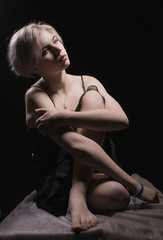 Fototapeta premium Beautiful blonde in black dress sitting on black background