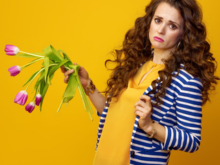 sad modern woman on yellow background holding wilted flowers